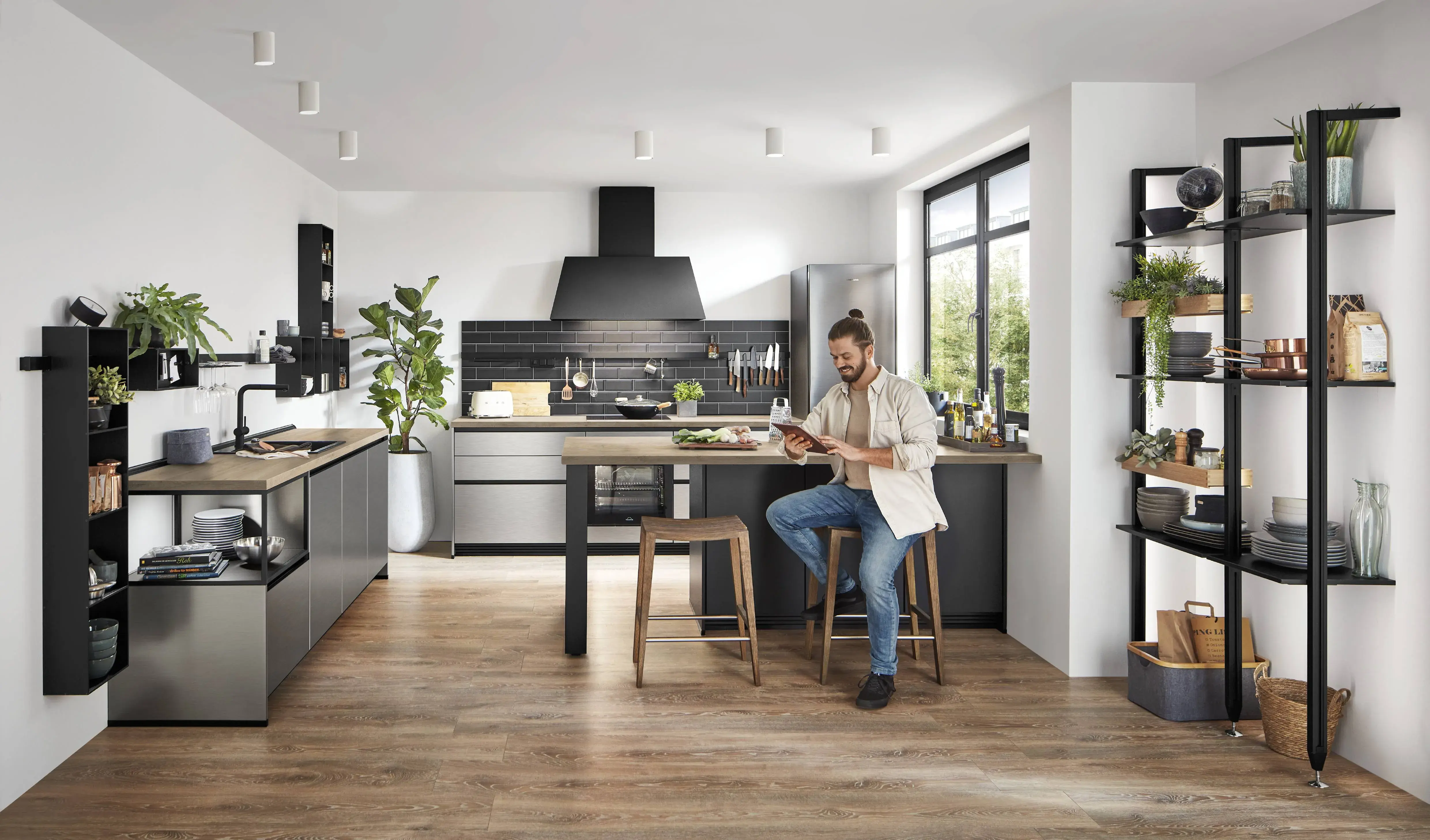 Nobilia Inox moderne Küche mit offenen Regalen Mann sitzt an Theke und schaut auf sein Tablet