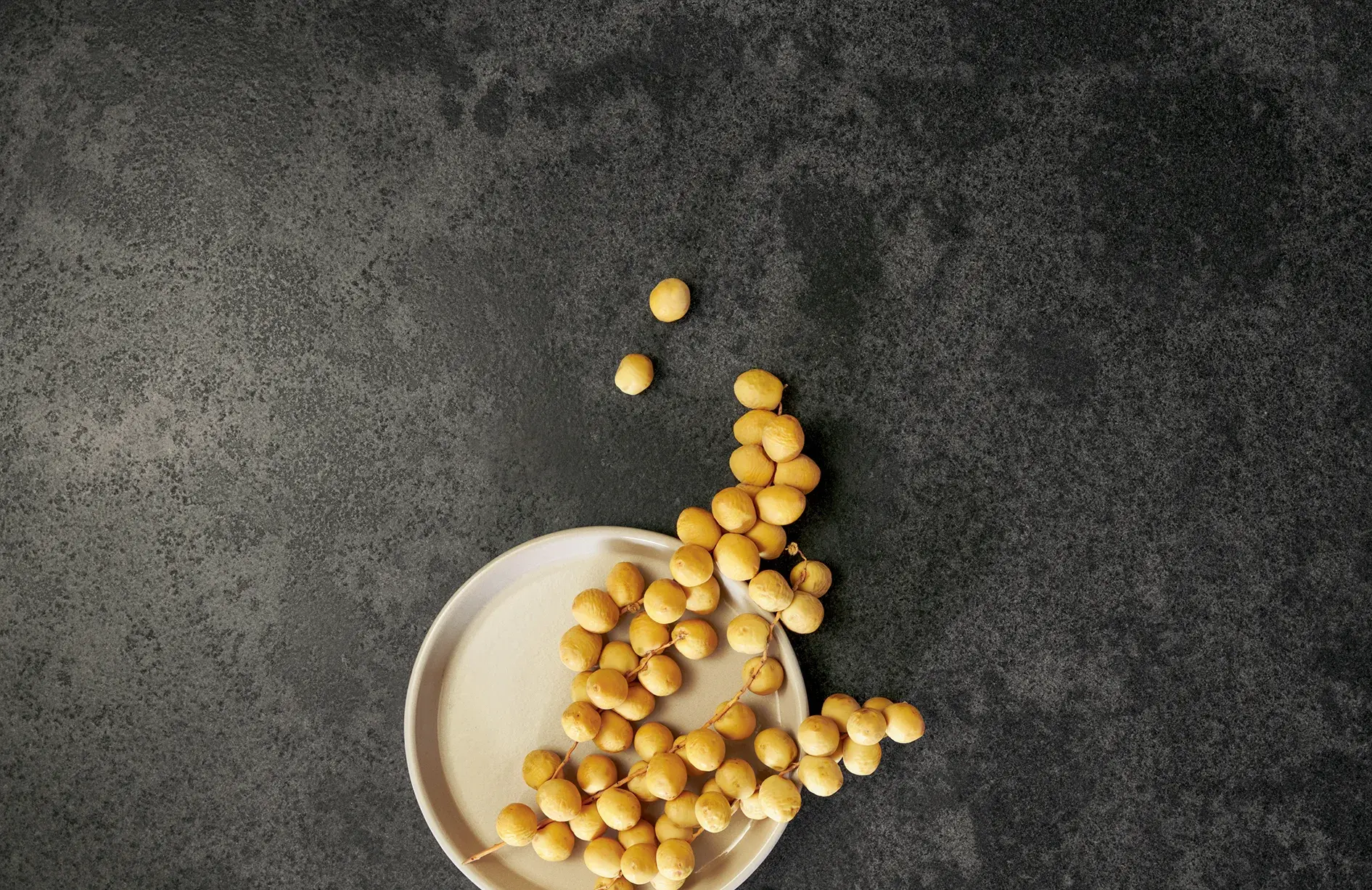 systemo dunkelgraue, fein gemaserte Natursteinarbeitsplatte Teller mit süßen runden gelben Datteln